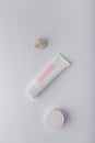 Cream tube with pink blank label, no brand mockup on white background with geometric concrete decor. Tender minimal composition