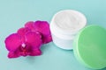 Cream in white jar with green cap on mint background with beautiful bright magenta orchid flowers. Soft cream with orchid extract Royalty Free Stock Photo