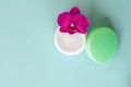Cream in white jar with green cap on mint background with beautiful bright magenta orchid flowers. Soft cream with orchid extract Royalty Free Stock Photo