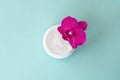 Cream in white jar on mint background with beautiful bright magenta orchid flowers. Soft cream with orchid extract for moisturizin Royalty Free Stock Photo