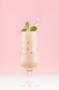 Creamy alcohol coffee cocktail with ice cubes, green mint and straw in elegant wineglass on white table and soft light pink wall. Royalty Free Stock Photo