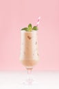 Creamy cold fresh beverage in elegant transparent glass with ice cubes, green mint and striped straw in modern light pink color.