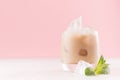 Creamy cold fresh beverage in misted glass with ice cubes, green mint and striped straw in modern light pink interior, copy space.