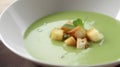 Creamy green soup with croutons and mint in a bowl