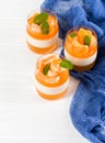 Creamy panna cotta with orange jelly in beautiful glasses, fresh ripe mandarin, blue textile on white wooden background. Delicious