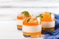 Creamy panna cotta with orange jelly in beautiful glasses, fresh ripe mandarin, blue textile on white wooden background. Delicious