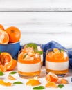 Creamy panna cotta with orange jelly in beautiful glasses, fresh ripe mandarin, blue textile on white wooden background. Delicious