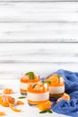 Creamy panna cotta with orange jelly in beautiful glasses, fresh ripe mandarin, blue textile on white wooden background. Delicious