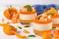 Creamy panna cotta with orange jelly in beautiful glasses, fresh ripe mandarin, blue textile on white wooden background. Delicious