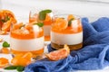 Creamy panna cotta with orange jelly in beautiful glasses, fresh ripe mandarin, blue textile on white wooden background. Delicious