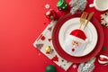 Top view of plates, whimsical gold flatware in pocket, napkin, mug, ornaments, snowflake confetti on red backdrop Royalty Free Stock Photo