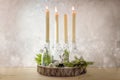 Creative Advent wreath, candles in bottles on a wooden board with fir branches and decoration against a light rustic wall, three