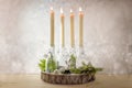 Creative Advent wreath, four lit candles in bottles on a wooden board with fir branches and decoration against a light rustic wall