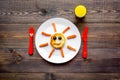 Creative approach to kid`s braekfast. Meal with cheesecake in shape of sun. Dark wooden background top view Royalty Free Stock Photo