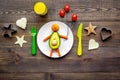 Creative approach to kid`s braekfast. Meal in shape of happy avocado man . Dark wooden background top view Royalty Free Stock Photo
