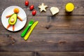 Creative approach to kid`s braekfast. Meal in shape of happy avocado man . Dark wooden background top view copyspace Royalty Free Stock Photo