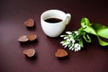 Creative arrangement of spring flowers, coffee cup and chocolate hearts on a dark background.