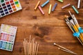 Creative art work accessories tools supplies set on messy desk, paint brushes, paintbox watercolors crayons pencils on brown Royalty Free Stock Photo