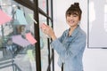 Creative Asian businesswoman post and writing ideas or tasks on sticky papers on glass wall in office. Korean or Japanese young Royalty Free Stock Photo