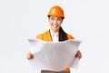 Creative asian female architect imaging her plan, standing in safety helmet and looking away thoughtful while reading