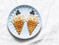 Creative baby food. Waffles with banana and blueberries on a light background, top view. Cheerful children`s food. Flat lay, copy