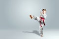 Creative background, a child in a white kimono makes a kick, on a light background. The concept of martial arts, karate