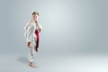 Creative background, a child in a white kimono makes a kick, on a light background. The concept of martial arts, karate