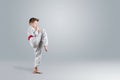 Creative background, a child in a white kimono makes a kick, on a light background. The concept of martial arts, karate