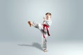 Creative background, a child in a white kimono makes a kick, on a light background. The concept of martial arts, karate