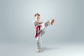 Creative background, a child in a white kimono makes a kick, on a light background. The concept of martial arts, karate