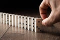 Creative background, Male hand pushing white dominoes, on a brown wooden background. Concept of domino effect, chain Royalty Free Stock Photo