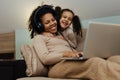 Creative black mother and daughter working on school project, using modern laptop