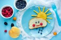 Creative breakfast idea for kids - bread bun with fruit and berry shaped funny cloud with peach sun and blueberry rain , fun with Royalty Free Stock Photo