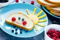 Creative breakfast idea for kids - bread bun with fruit and berry shaped funny cloud with peach sun and blueberry rain Royalty Free Stock Photo