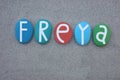 Creative celebration of Freya, feminine given name composed with multi colored stone letters over beach sand