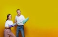 Creative cheerful man and woman holding household tools on yellow studio wall background. Housekeeping and cleaning service