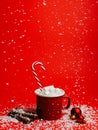 Creative Christmas composition with snow falling, tea cup, marshmallow drink and cinnamon sticks on red background. Minimal Xmas e Royalty Free Stock Photo