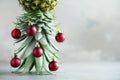 Creative Christmas tree made of pineapple and red bauble on grey concrete background, copy space. Greeting card, decoration for Royalty Free Stock Photo