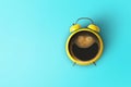 Creative coffee with a smile and a yellow alarm clock on a blue background. Concept idea of a happy wake up in the morning. Royalty Free Stock Photo