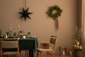 Creative composition of christmas living room interior with table, chair, candle with candlestick, glass tabrewere, brown wall and