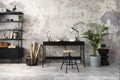 Creative composition of concrete interior of home office with black desk, simple rack, wooden stool, plant in flowerpot, basket, Royalty Free Stock Photo