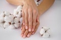 Hands of a young woman on white cotton flowers on a white background. Female manicure. Cotton flower. Close-up