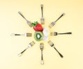 Creative composition in the form of the sun made of forks arranged around a tiny plate with a piece of banana, kiwi, strawberry