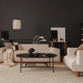 Creative composition of living room interior with modular beige sofa, black coffee table, armchair, rug, black wall with stucco,