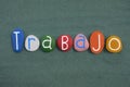 Trabajo word meaning work in spanish language composed with multi colored stone letters over green sand Royalty Free Stock Photo