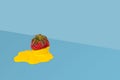 Creative composition with ripe strawberry and yellow melting cream on bright blue background