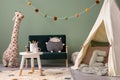 Creative composition of stylish and cozy child room interior design with greeen wall, plush toys, hut, bottle green sofa, Royalty Free Stock Photo