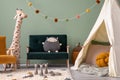 Creative composition of stylish and cozy child room interior design with greeen wall, plush toys, hut, furniture and accessories.