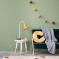 Creative composition of stylish and cozy child room interior design with green wall with bottle greeen sofa, plush pilow, bright