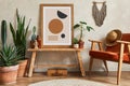 Creative composition of stylish living room interior with mock up poster frame, armchair, cacti and personal and boho accessories.